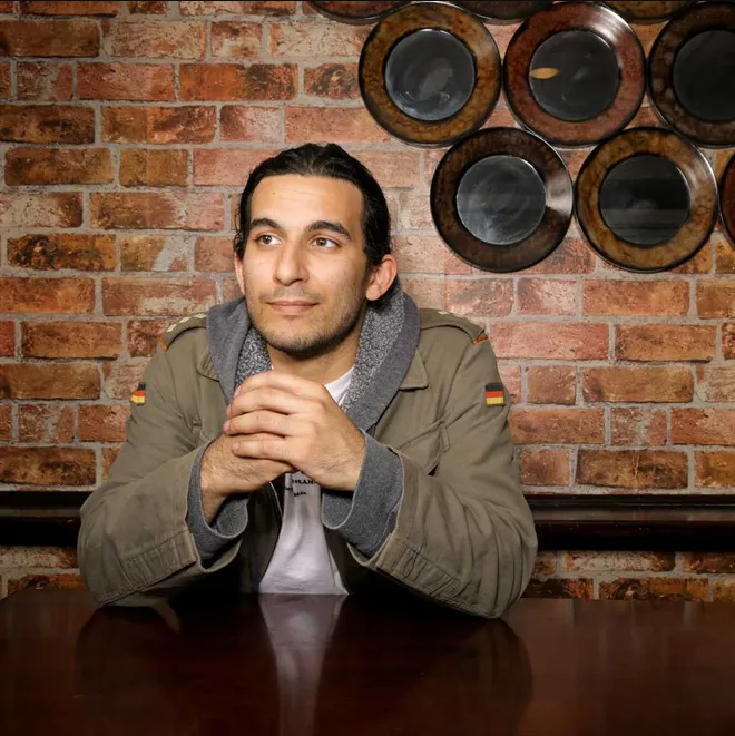 Imran Stanton Cooper, photographed in front of brick wall and dishware for The Florida Times-Union, February 15 2015, Matt Soergel byline. The same source photo anchors The Full Arc memoir cover.