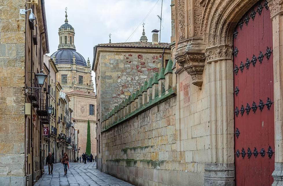 A cobbled street beside the old University of Salamanca, its carved stone gate and dome beyond